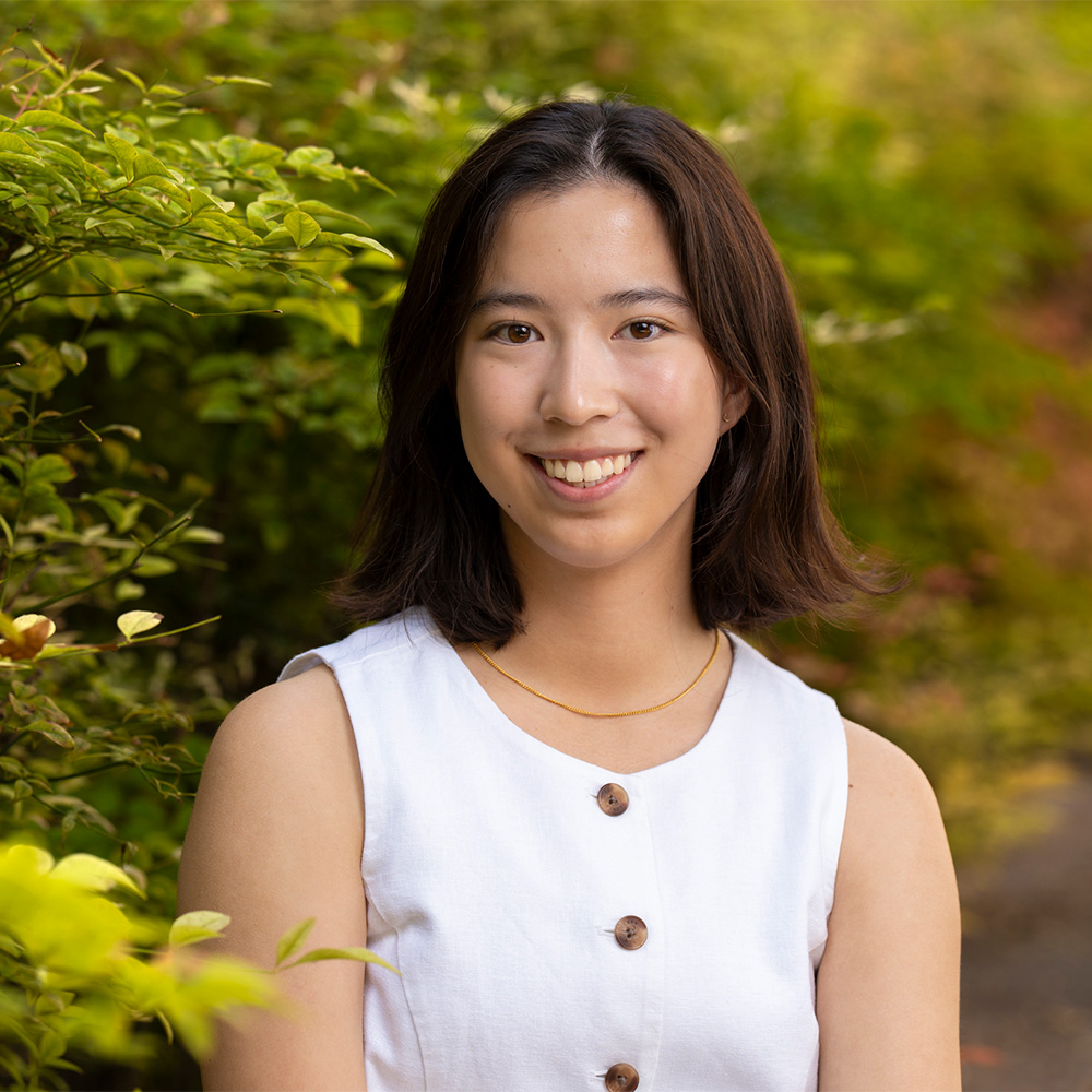 Smiling young woman in white buttoned top by green foliage, portrait