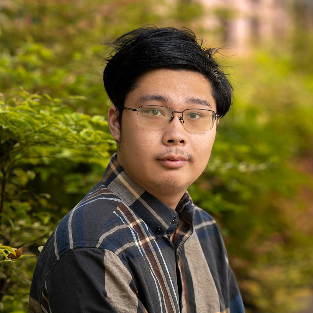 Portrait photo of a young person with glasses in a striped shirt against green foliage