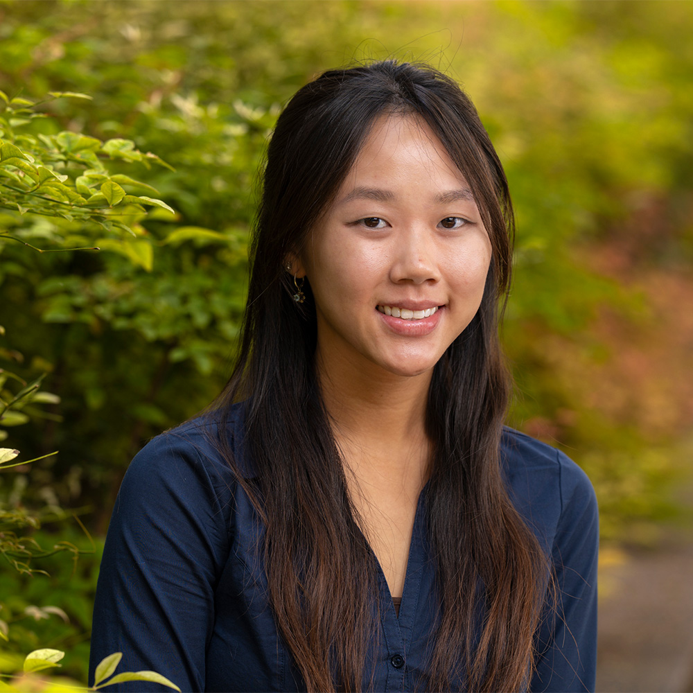 Smiling young woman with long dark hair in navy blouse, head-and-shoulders portrait outdoors