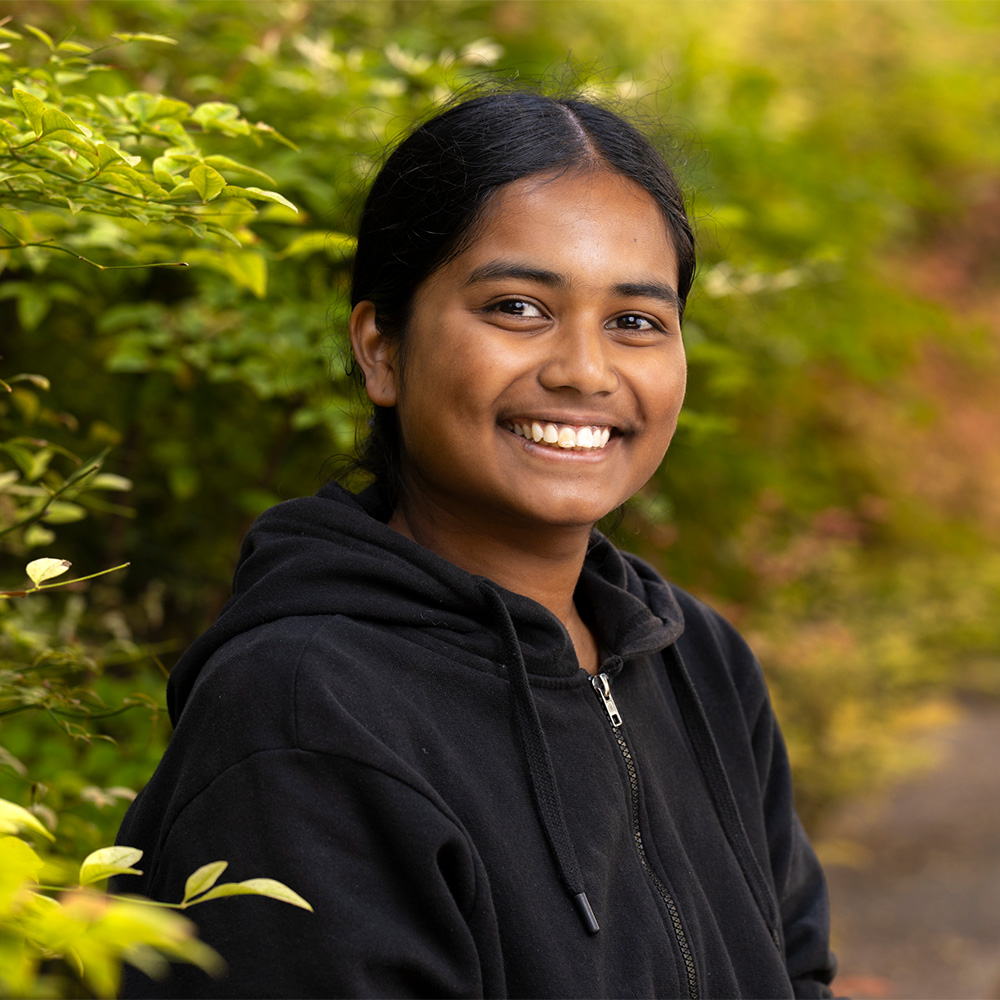 Smiling young woman in a black hoodie by leafy bushes, outdoor portrait photo