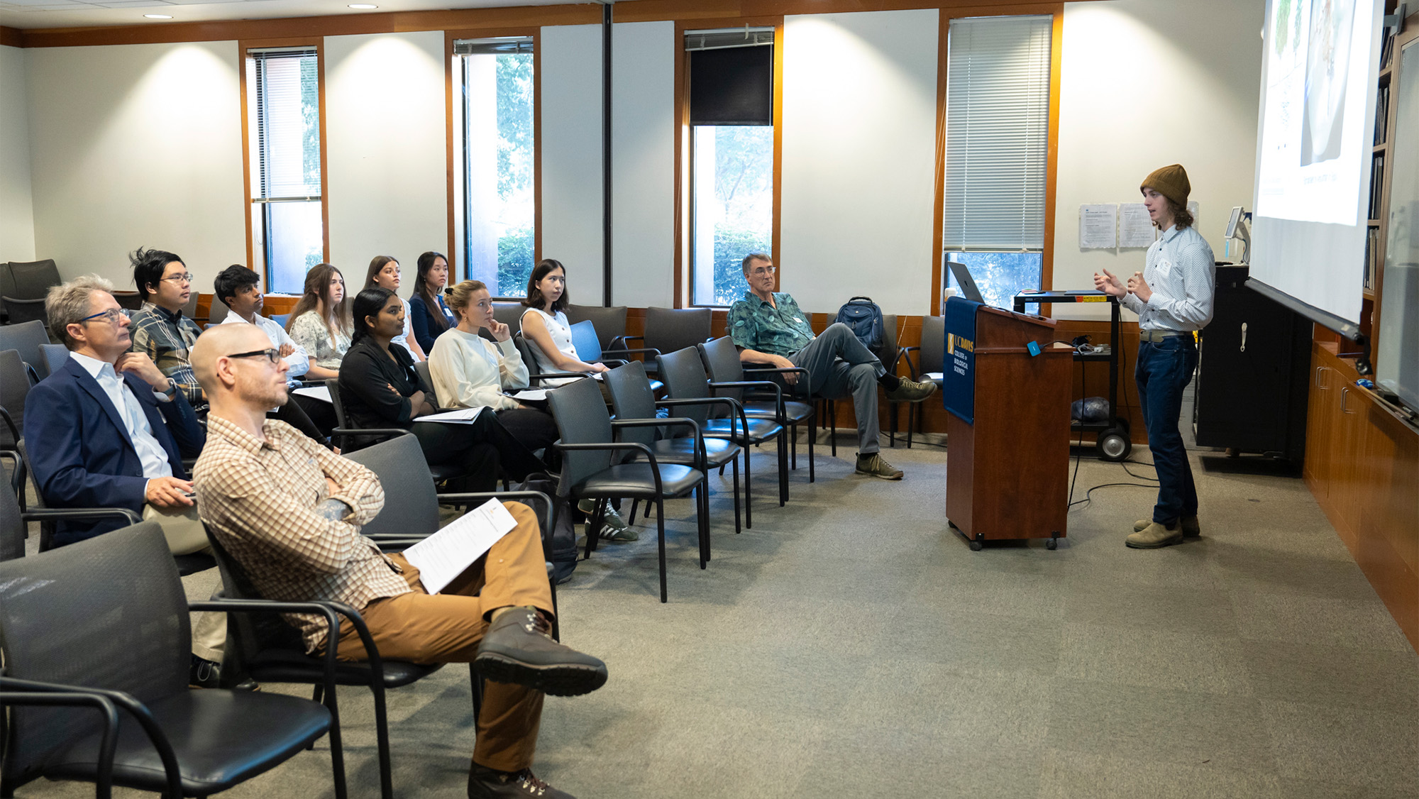 Conference room presentation: standing speaker at lectern addressing seated, attentive audience