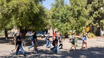 Group of students walks across campus, led by a guide holding a bright sign for the “Marine & Coastal Science” program.