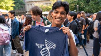 Smiling attendee proudly displays a blue T-shirt from the UC Davis biological sciences program amid a busy campus crowd.