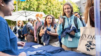 Wearing a backpack, a student flashes a thumbs-up after receiving a DNA-themed shirt from the College of Biological Sciences.