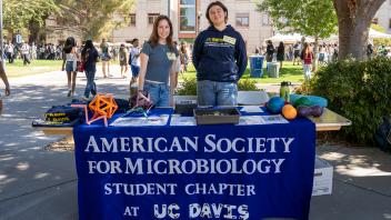 Two people standing in front of a table with a blue banner on it