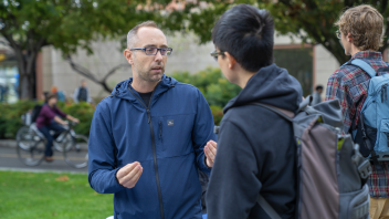 Two people converse on the UC Davis quad during the Graduate Student Fair, with bikes and trees in the background.