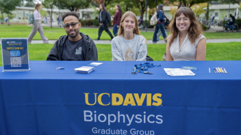 Three people sit behind a UC Davis Biophysics Graduate Group table at the campus Grad Student Fair.