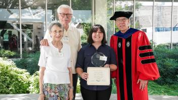 Scholarship recipient poses with award, surrounded by smiling family and faculty outside UC Davis building after ceremony.
