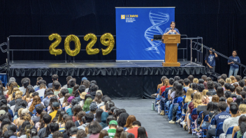 A speaker at the podium addresses the new class of 2025 in front of a blue CBS backdrop.