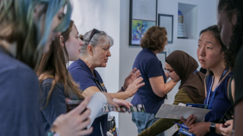 Students engage with UC Davis staff at an indoor booth, receiving materials and asking questions during orientation.