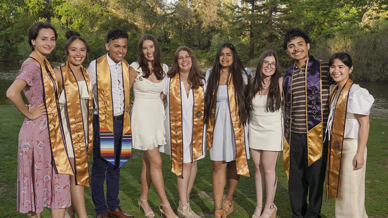 Group of students wearing their graduation stoles standing outside and smiling. 
