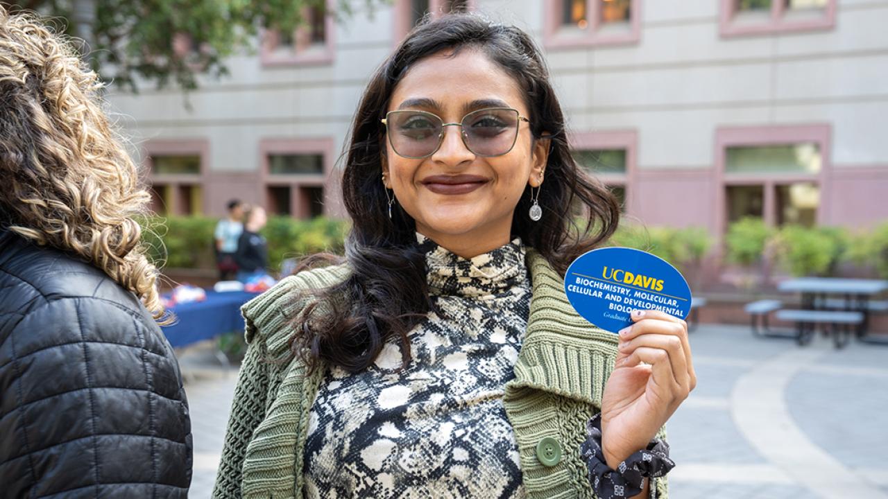 A person with long black hair holding a UC Davis sticker
