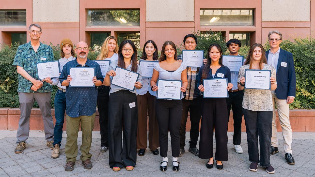 Diverse group holding certificates, smiling outside a brick building (photo)