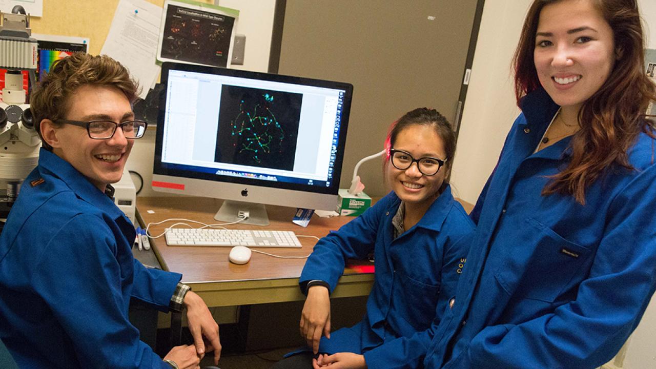 Three students in lab next to computer