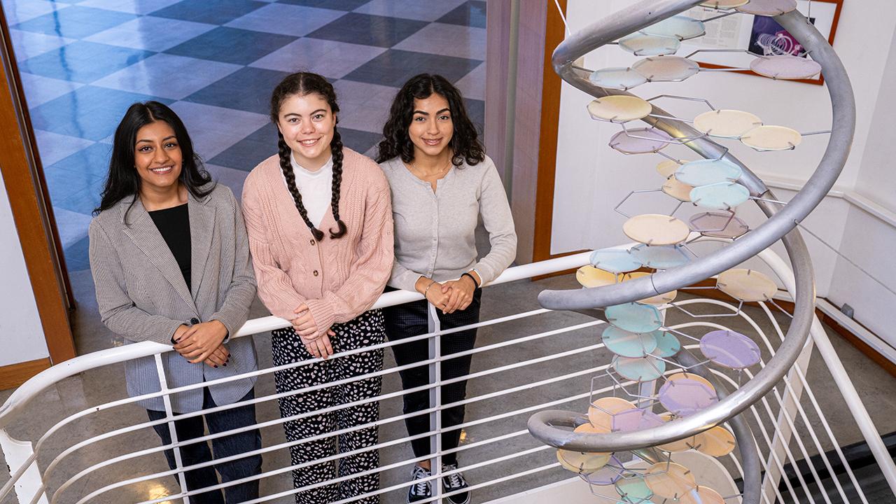 Three female students gathered in front of the DNA helix sculpture