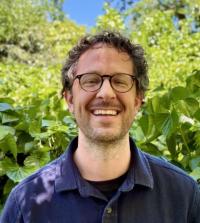 A person with curly hair and glasses standing outside