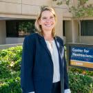 Smiling woman in blazer stands outside UC Davis Center for Neuroscience building beside center’s sign.
