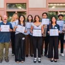 Diverse group holding certificates, smiling outside a brick building (photo)