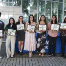 Seven UC Davis students stand in a row holding certificates after receiving the 2025 Norma J. Lang Prize for Undergraduate Information Research. They are smiling and posed in front of the UC Davis Library entrance, with a podium and a poster honoring Norma J. Lang visible in the background.