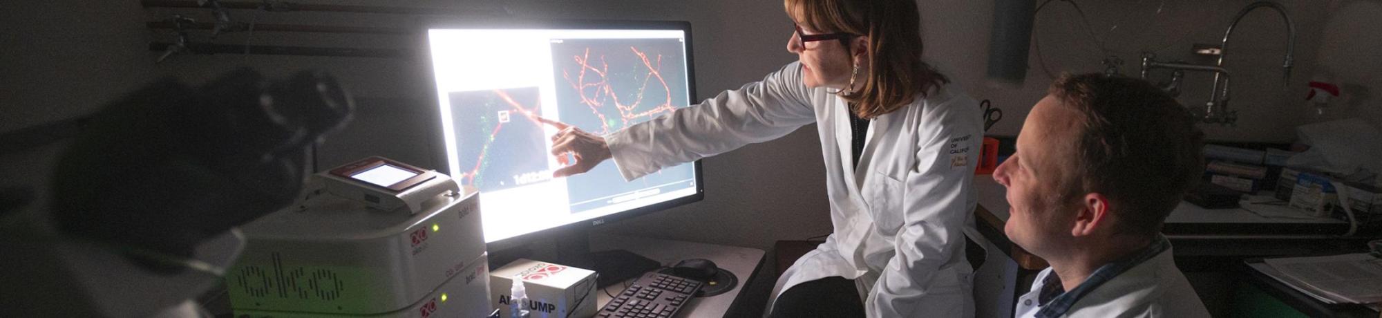 Male and female researcher in white coats in dark room before illuminated screen