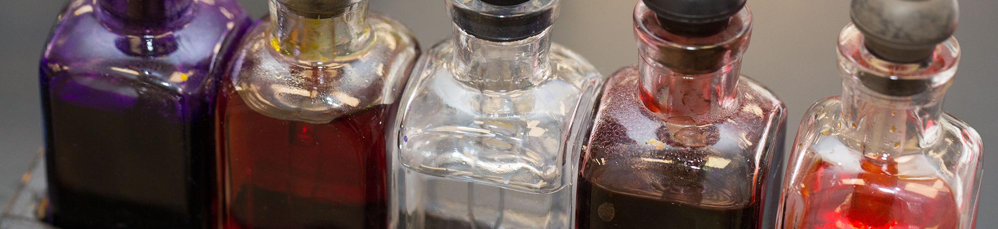 Row of clear glass bottles containing liquids of different colors